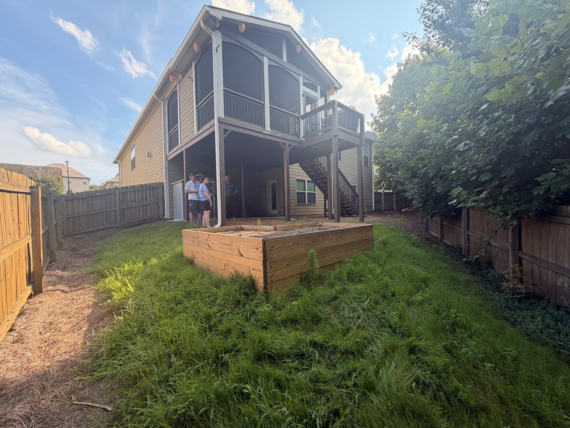 Before: overgrown backyard with tall weeds, a raised garden bed and unusable ground beneath an elevated deck