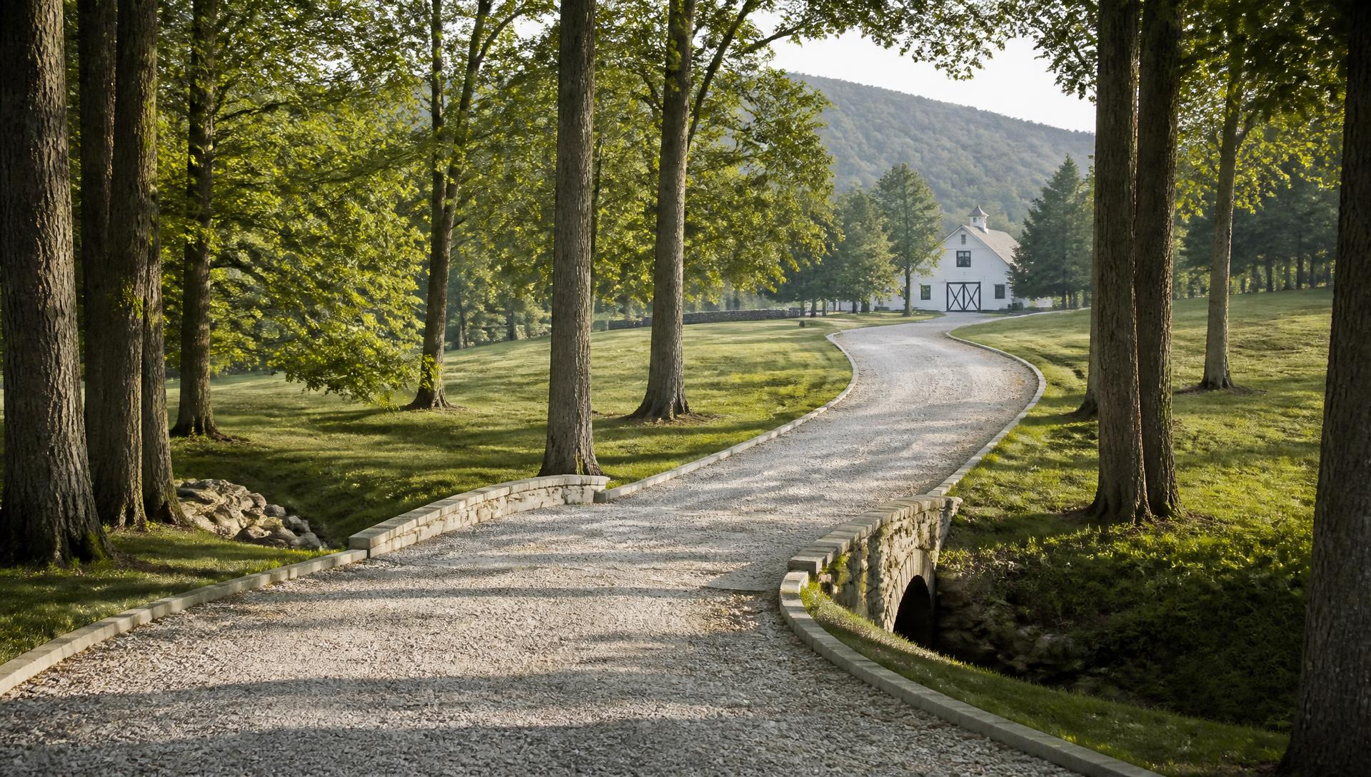 Gravel estate driveway curving through hardwoods toward a white barn